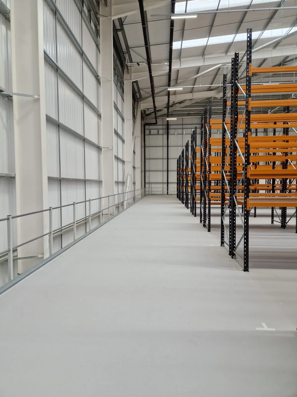 A guardrailed mezzanine walkway running beside runs of pallet racking in a new warehouse.
