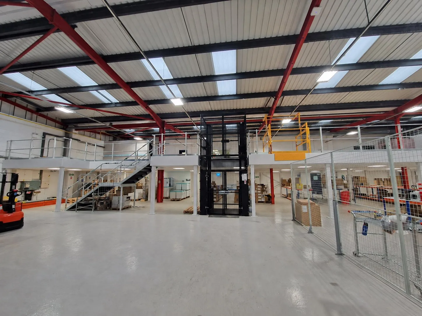 A steel mezzanine floor with a staircase, goods lift and pallet gate in a warehouse unit