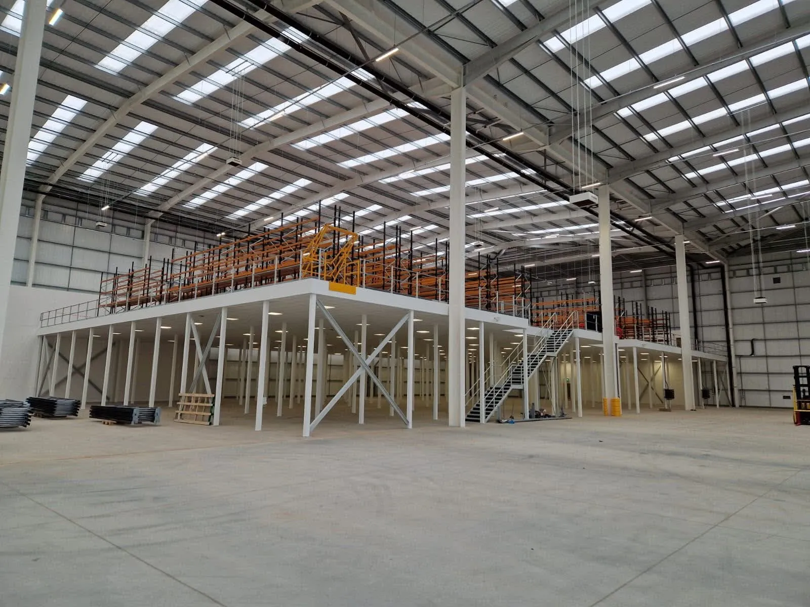 A steel mezzanine floor on columns spanning a warehouse unit, with racking on the deck and a staircase down