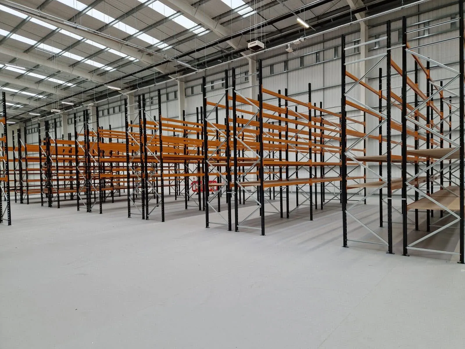 Tall runs of shelving bays, some fitted with timber shelf levels, in an empty warehouse